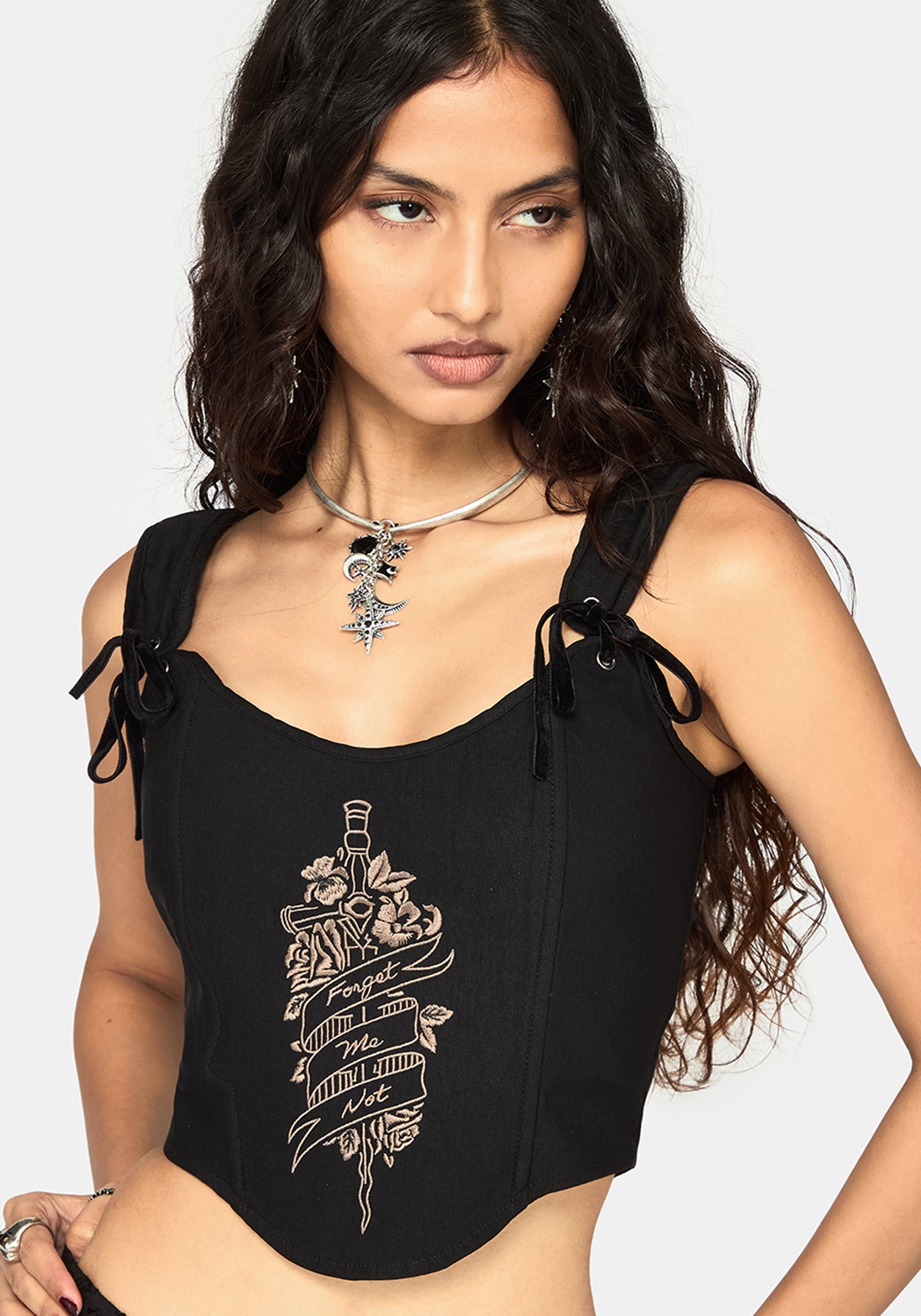 A woman wearing a black sleeveless corset top with side tie details and a beige graphic print on the front, photographed against a light gray studio background.